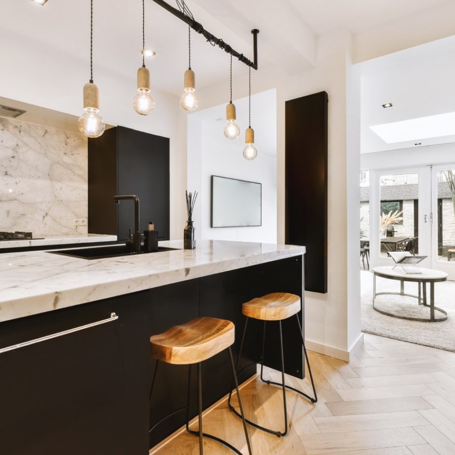 a modern kitchen with marble counter tops and black cabinetry in the room is lit by two pendants hanging over the island